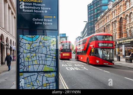 Iconic red London double decker buses seen on Tottenham Court Road. A sign with maps gives directions for tourists, Stock Photo