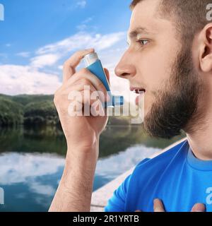 Man using asthma inhaler near lake. Emergency first aid during outdoor recreation Stock Photo