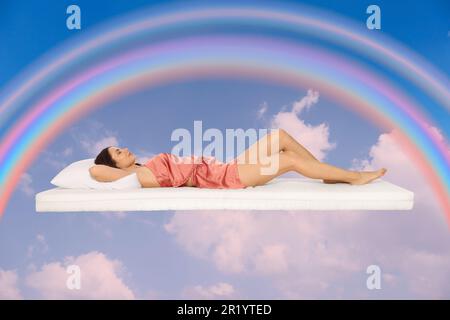 Sweet dreams. Young woman lying on mattress in blue sky with bright rainbow Stock Photo