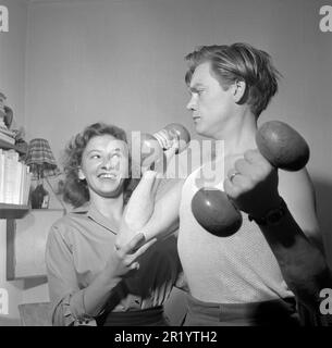 Fun in the 1950s. a man exercises with a pair of dumbbells and his wife stands by his side and watches.  He is actor Lars Ekborg, 1926-1969 and Lola Sjölund 1925-2015. Sweden 1951.  Conard ref 1754 Stock Photo
