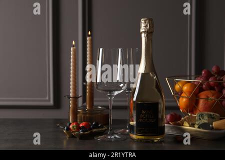Bottle of sparkling wine, glasses, candles and delicious snacks on grey table Stock Photo