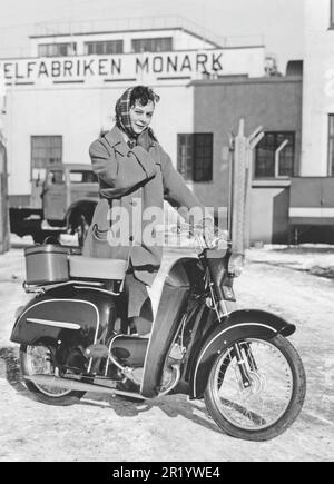 A young woman sitting on the company Monark's new product Monarscoot presented to the press in 1956. One of the mopeds of the time that stands out in terms of appearance and has a Vespa-like appearance. Monarscoot was manufactured by Monark in Varberg between 1957 and 1969. It had two gears and was launched as cheap to buy, SEK 945, cheap to operate. Stock Photo