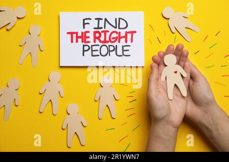 Find the right people. Woman choosing human paper figure with drawn heart among others without it on yellow background, top view Stock Photo