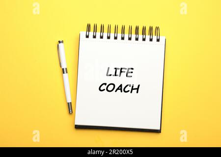 Phrase Life Coach written in notebook and pen on yellow background, top view Stock Photo