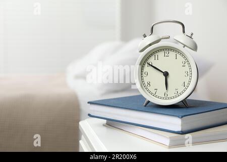 Alarm clock and books on white nightstand in bedroom, space for text Stock Photo