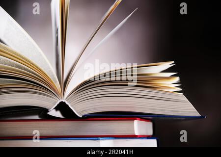 A composition with an open hardcover book lying on a stack of other books Stock Photo