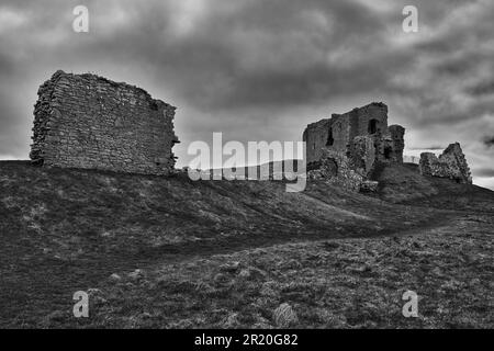 The ancient Duffus castle ruins atop a rocky hill, surrounded by clouds and overcast skies Stock Photo