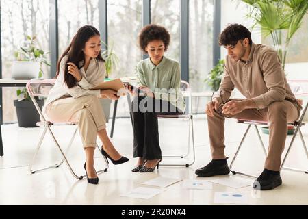 Three Diverse Colleagues Sitting Looking At Business Papers In Office Stock Photo