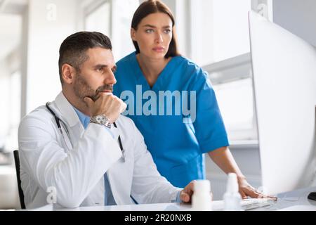 Diagnosis discussion. Focused male doctor and his assistant analyzing medical conditions using computer in clinic Stock Photo