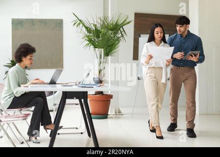 Three Business Professionals Working Using Computers, Reading Papers In Office Stock Photo