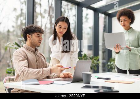 Serious Multicultural Coworkers Pointing At Laptop Discussing Problems In Office Stock Photo