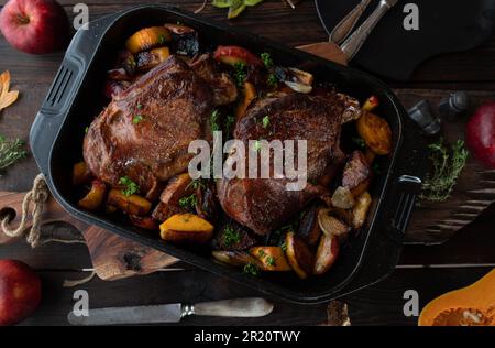 Meat dish for thanksgiving with roasted turkey shanks. Served with butternut pumkin, red apples, onions in roasting pan on rustic and wooden table Stock Photo