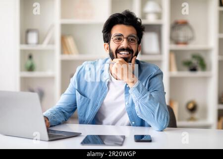 Dreamy indian freelancer man sitting at desk in home office Stock Photo