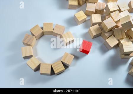 Many wooden cubes, some of them together forming a circle with a gap, one in red color is ready to complete the team, light blue background, copy spac Stock Photo