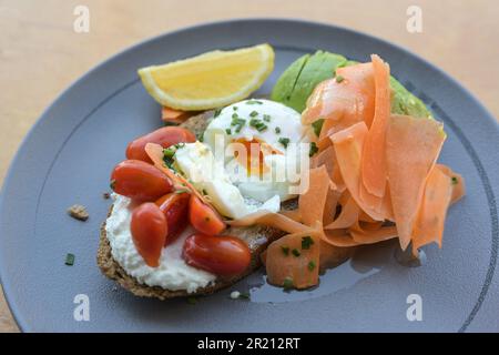Healthy breakfast or lunch sandwich with rye bread, cream cheese, tomatoes, boiled egg, avocado and thinly sliced carrots served on a blue plate, sele Stock Photo