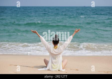 Young woman sitting on sea beach enjoying sound of waves Stock Photo