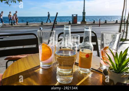 Refreshing drinks in drinking glasses and bottles on a table in a seaside street cafe, blurry people walking on the promenade at the waterfront on a s Stock Photo