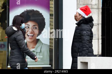 A shopper wearing a mask and a Santa hat walks along Hornchurch high street in the London Borough of Havering amid the COVID-19 coronavirus pandemic as a new COVID-19 variant known as B.1.1.529 or Omicron continues to spread 2021. Stock Photo