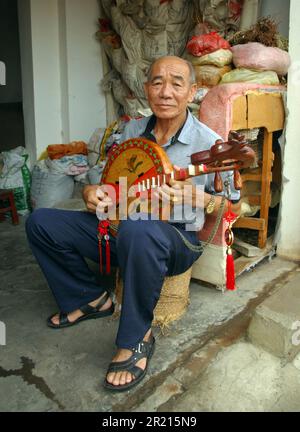 A man plays a Sanxian, a three stringed instrument, at a market in Kaiyuan, Yunnan, China Stock Photo
