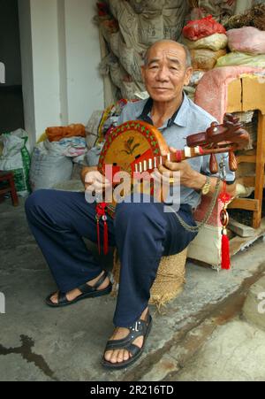 A man plays a Sanxian, a three stringed instrument, at a market in Kaiyuan, Yunnan, China Stock Photo