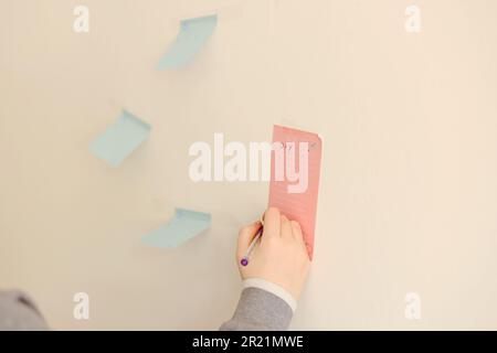 woman hand writing with colored sheets sticky note paper on white board background in home office Stock Photo