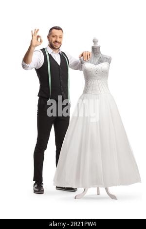 Tailor standing next to a bridal gown on a doll mannequin and gesturing great isolated on white background Stock Photo