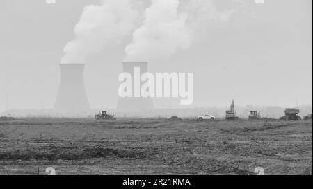 A grayscale shot of construction vehicles with silhouettes of towers in the background. Stock Photo