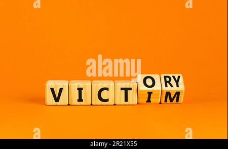 From victim to victory symbol. Businessman turns wooden cubes and changes concept words Victim to Victory. Beautiful orange background. Business suppo Stock Photo