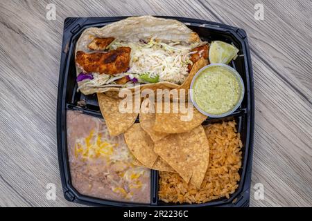 Overhead view of to go order of halibut fish taco meal with beans and chips all served in plastic container with dressing on the side. Stock Photo