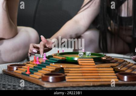 A close-up shot of the hands of two Latina friends as they move their game pieces on the Parques board. Stock Photo