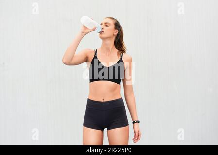 Hydration comes first. an attractive young female athlete drinking water against a grey background. Stock Photo