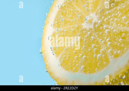 Lemon slice in water with bubbles on blue background Stock Photo