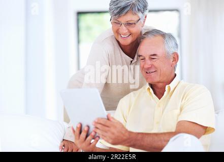 Couple using digital tablet at home. Cheerful mature couple smiling while using digital tablet at home. Stock Photo