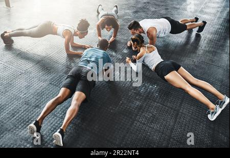 Planking is a full body experience. a group of young people doing planks together during their workout in a gym. Stock Photo