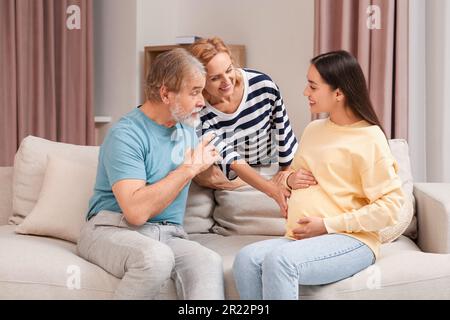 Happy pregnant woman spending time with her parents at home. Grandparents' reaction to future grandson Stock Photo