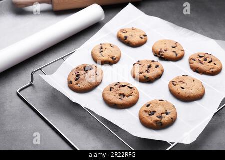 Roll of parchment baking paper and cooling rack with tasty cookies on dark grey table Stock Photo