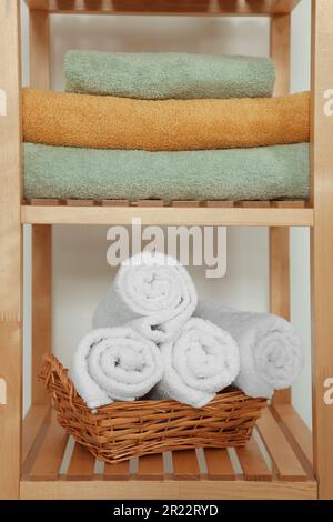 Soft folded towels in wicker basket on wooden shelving unit Stock Photo