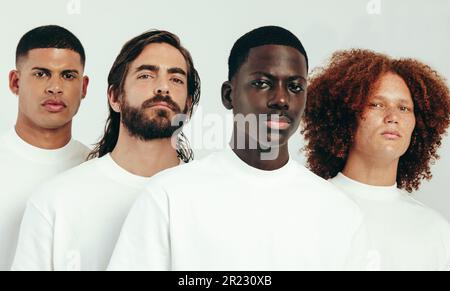 Group of young men with unique skin types standing together in a studio, looking at the camera. Youthful men representing diversity and male skincare Stock Photo
