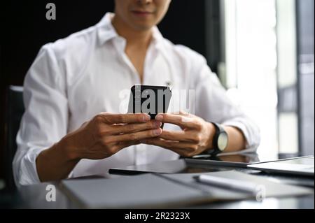 Close-up image of an Asian businessman chatting or sending sms to someone on his phone while sitting in his office. Stock Photo