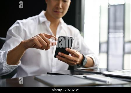 Close-up image of a businessman checking messages on hias smartphone at his desk in the office. Stock Photo