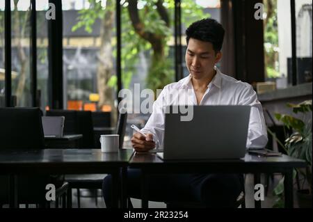 Focused and professional millennial Asian businessman working on his work, remote working at a coffee shop on the afternoon. Stock Photo