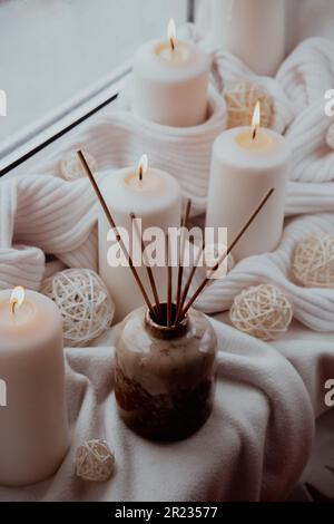 Aroma reed diffuser. Bottle container with wood stick diffusers Essential oils to scent your home fragnance concept autumn holidays at cozy home on the windowsill Hygge aesthetic atmosphere on knitted white sweater. Still life of micro moment candid slow living. Mental health wellbeing exercises Raining Outside Stock Photo