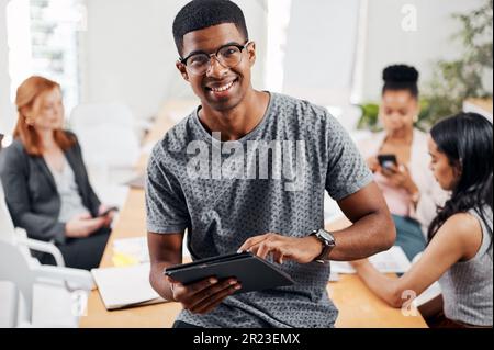 Talk about doing tasks with the most efficiency. Portrait of a young businessman using a digital tablet in an office with his colleagues in the Stock Photo