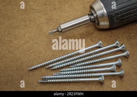Wood screws and electric drill on top of the brown MDF board Stock Photo