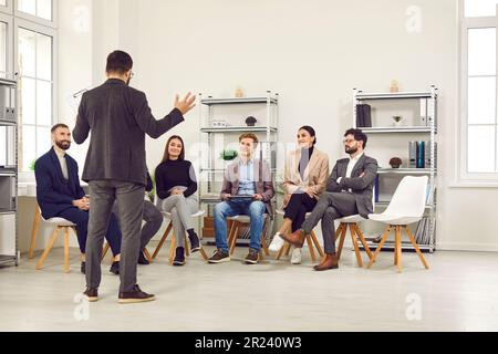 Small team of business people are listening to male speaker speaking in front of them in office. Stock Photo