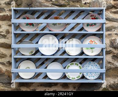 Old moldy and ornate enamel plates lined up on wooden shelf Stock Photo