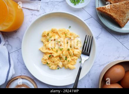 Scrambled eggs in a white plate of marble table - Flat lay of breakfast with orange juice and toast on the side Stock Photo