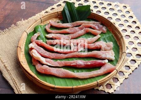 Sun Dried pork sliced( Uncooked) in bamboo tray of wood table - Thai food called Moo Dad Deaw Stock Photo