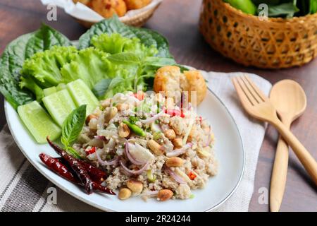 Yam Naem Khao Tod:  Thai fermented Spicy pork Salad with Crispy Rice ball at close view with vegetables on the side - Flat lay Thai appetizer food Stock Photo