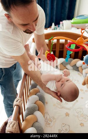 A happy father puts his child in a crib. A loving father holds his child in his arms tenderly and carefully Stock Photo